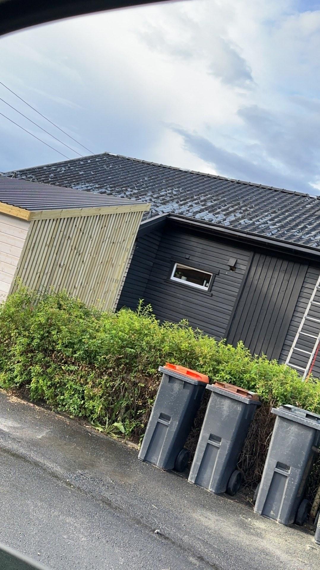 Søppelskur i tre med takpapp, ved en mørk bolig