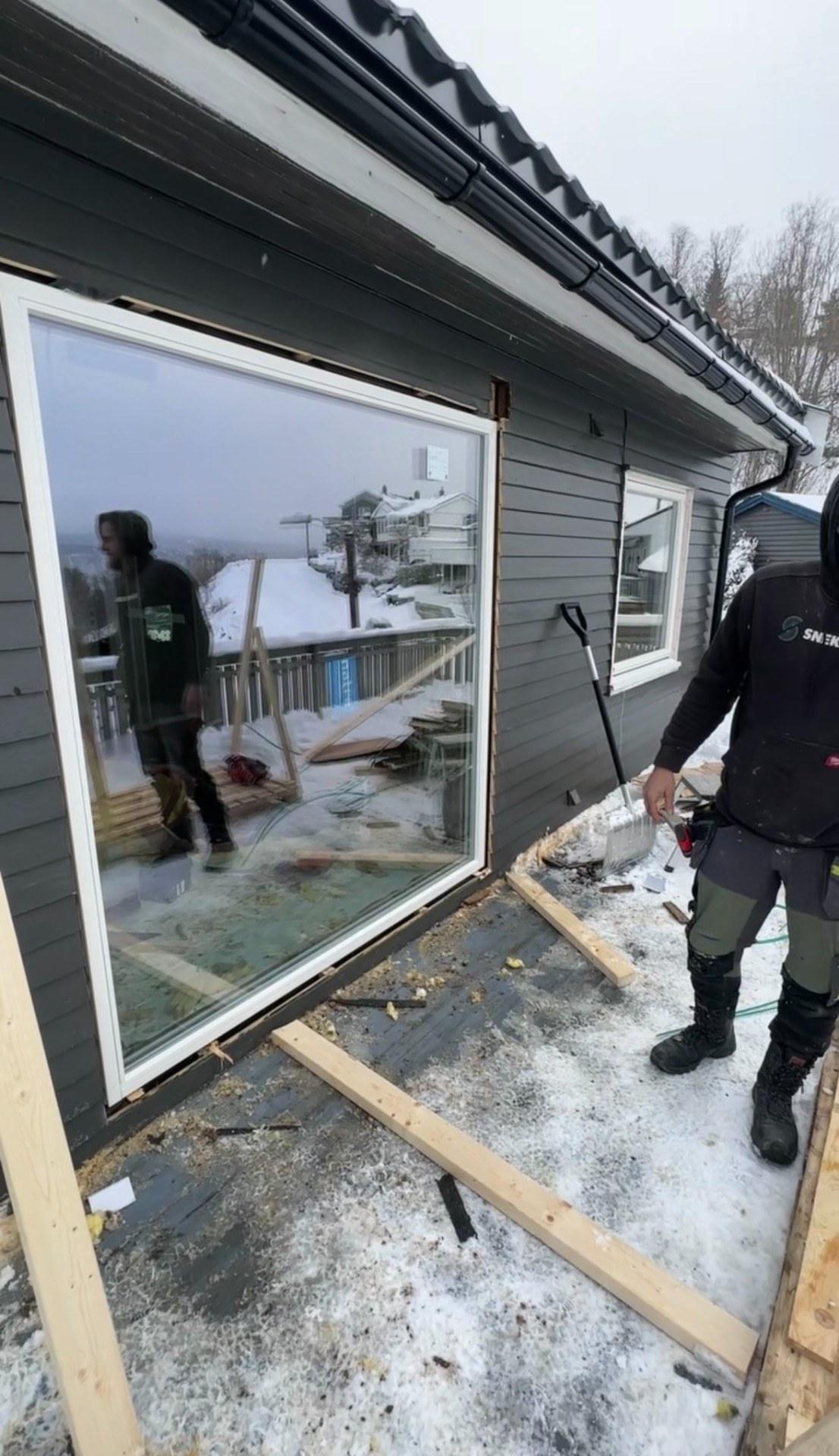 Et stort nytt vindu på plass i en mørk fasade, med snø på bakken